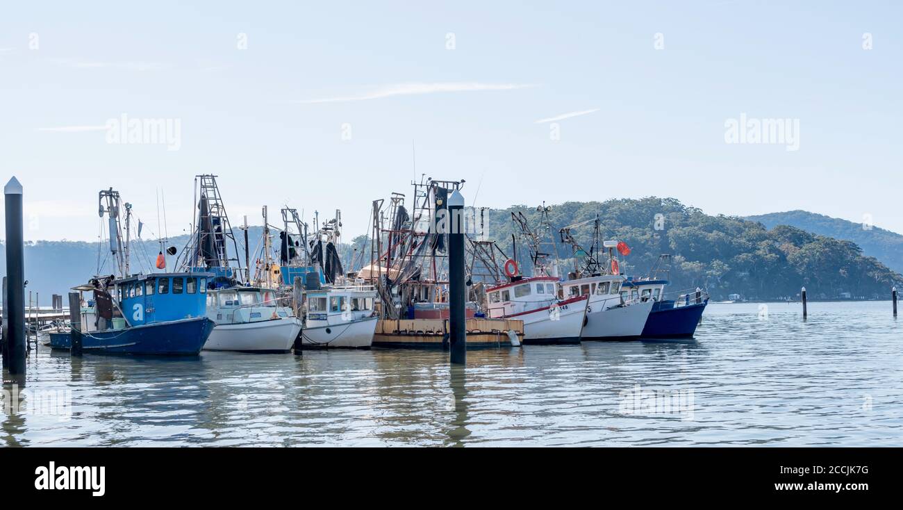 Avec l'île Dangar et Little Wobby en arrière-plan, une ligne de chalutiers de pêche en activité s'amarre à Brooklyn, en Nouvelle-Galles du Sud, en Australie Banque D'Images