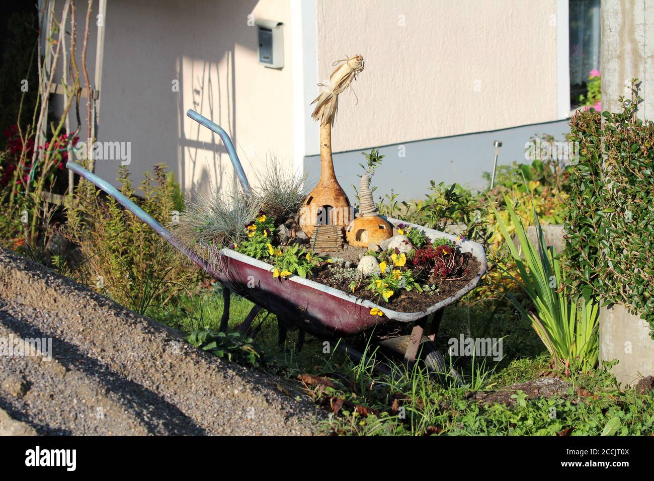 Chariot de construction de brouette rétro en métal d'époque rempli de terre et diverses fleurs mélangées à de la courge sèche sculptée et utilisées comme décoration de jardin Banque D'Images