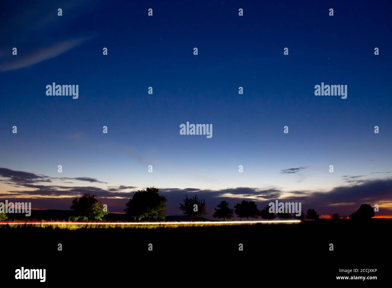 Phares d'une voiture roulant sur une route de campagne pendant le coucher du soleil, longue exposition Banque D'Images