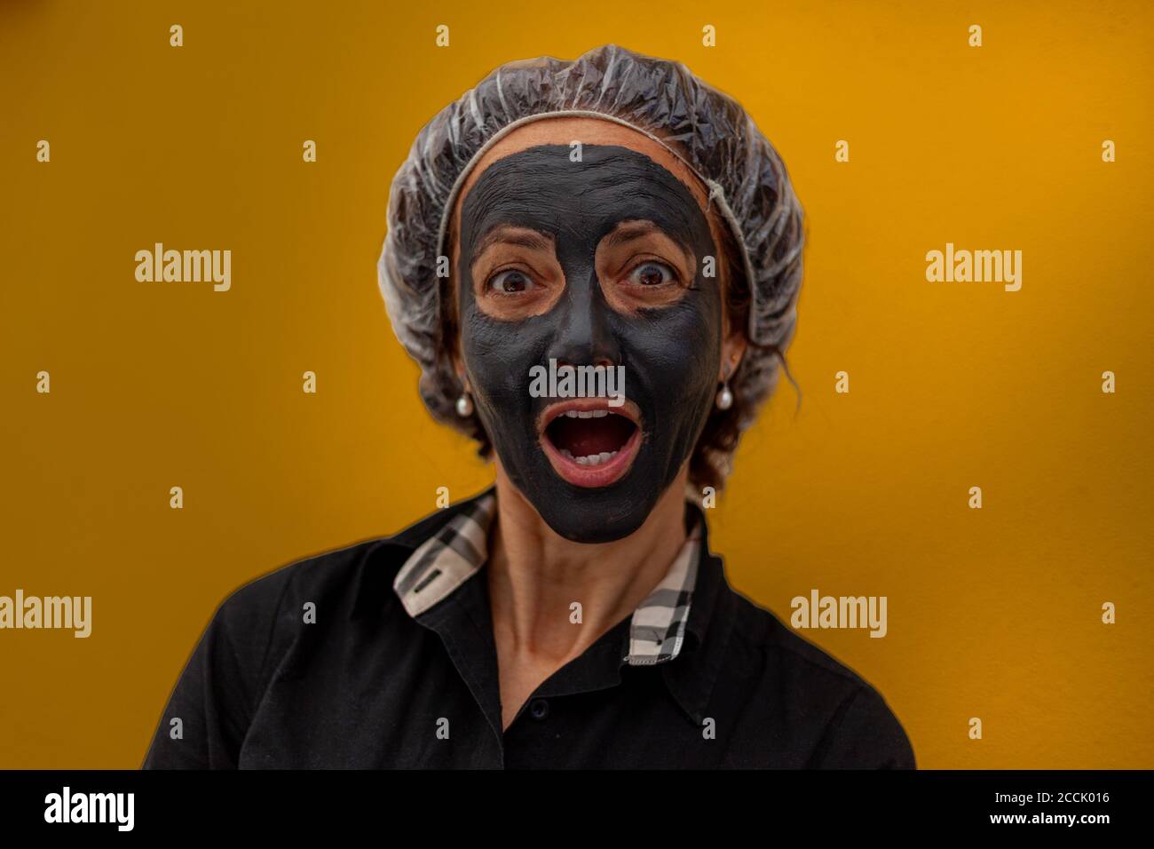 Femme brésilienne avec expression surprise et masque d'argile gris Banque D'Images