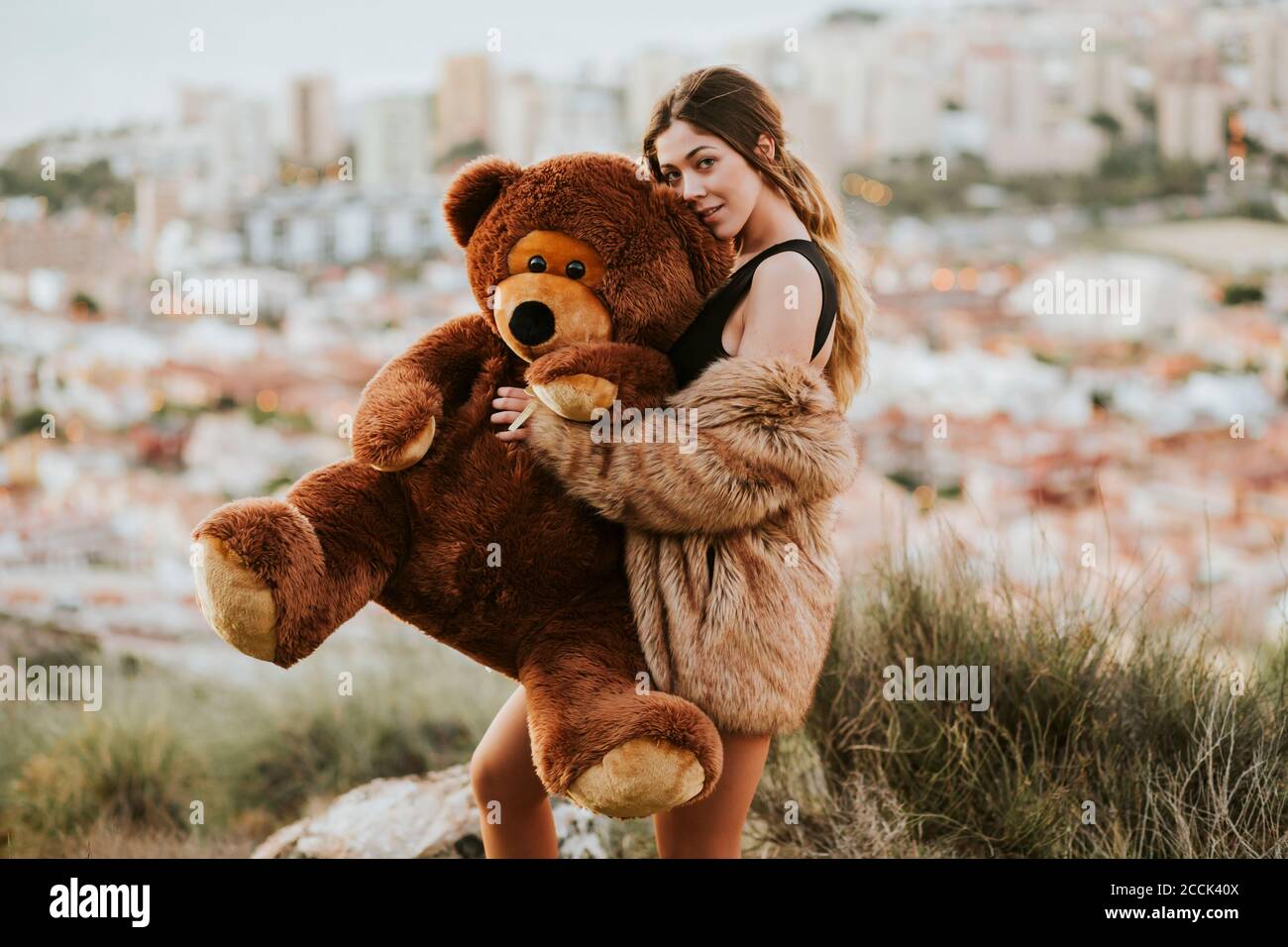 Jeune femme embrassant l'ours en peluche alors que la ville est en arrière-plan Banque D'Images