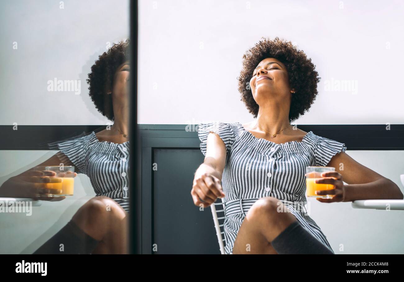 Femme détendue tenant un verre de jus d'orange tout en étant assise chaise sur le balcon de l'appartement de grand standing Banque D'Images