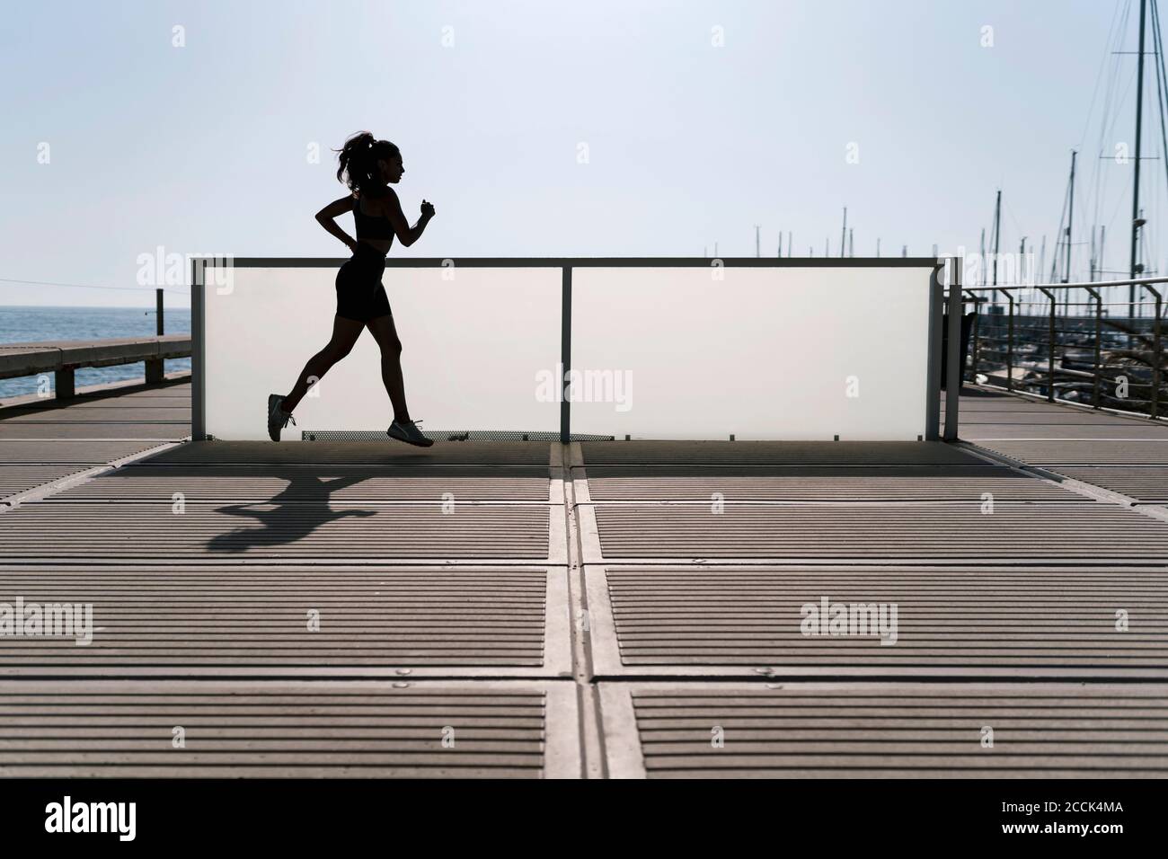 Femme sautant dans le port contre un ciel dégagé pendant la journée ensoleillée Banque D'Images