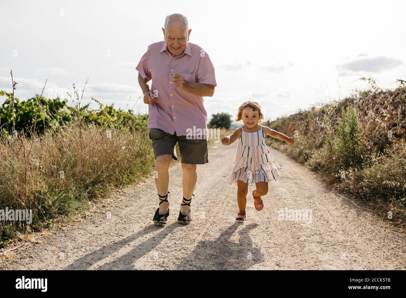 Un homme espiègle qui court avec sa petite-fille sur une route de terre au milieu plantes Banque D'Images