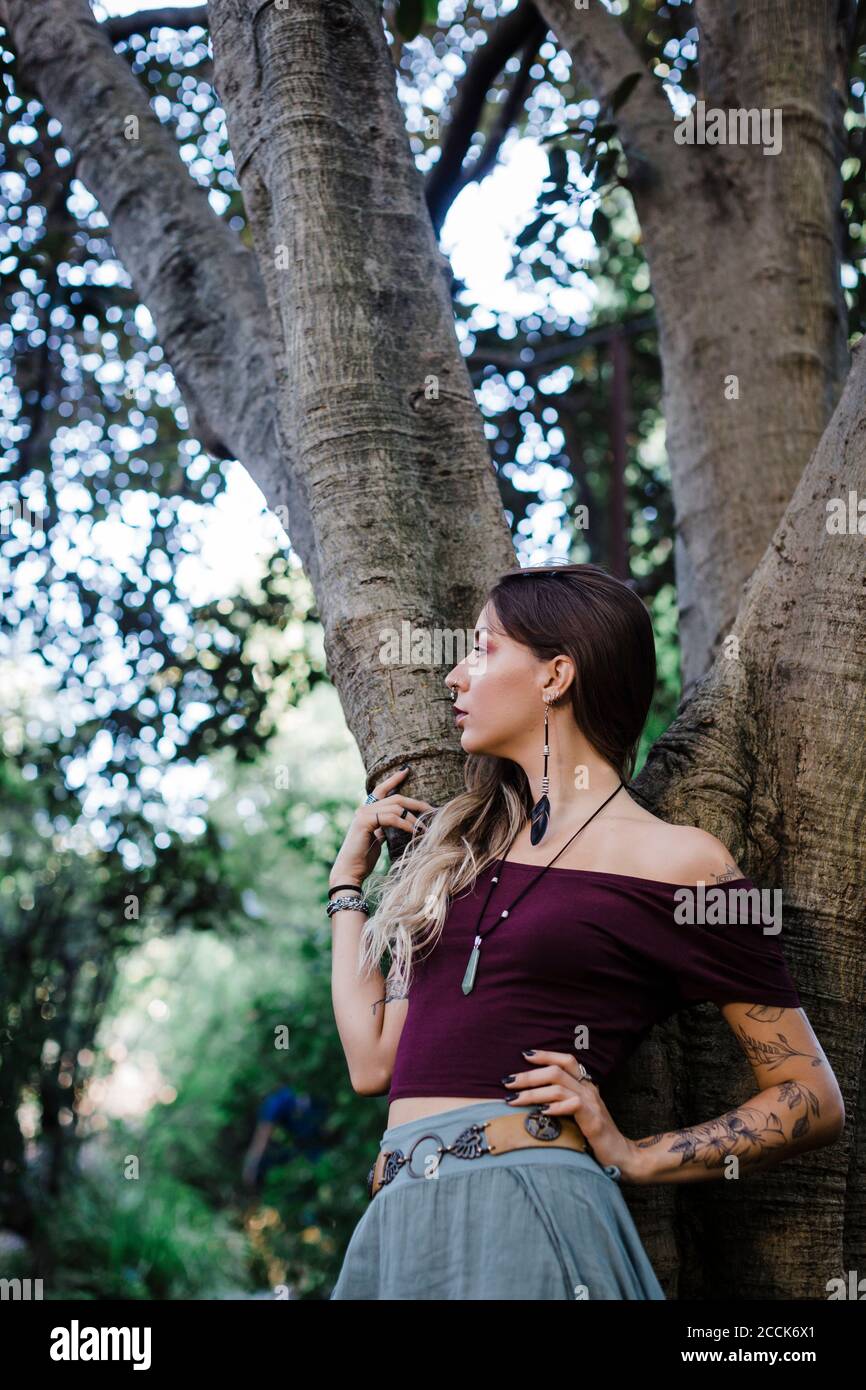 Portrait d'une jeune femme penchée sur un arbre et regardant latéralement vers l'intérieur stationnement Banque D'Images