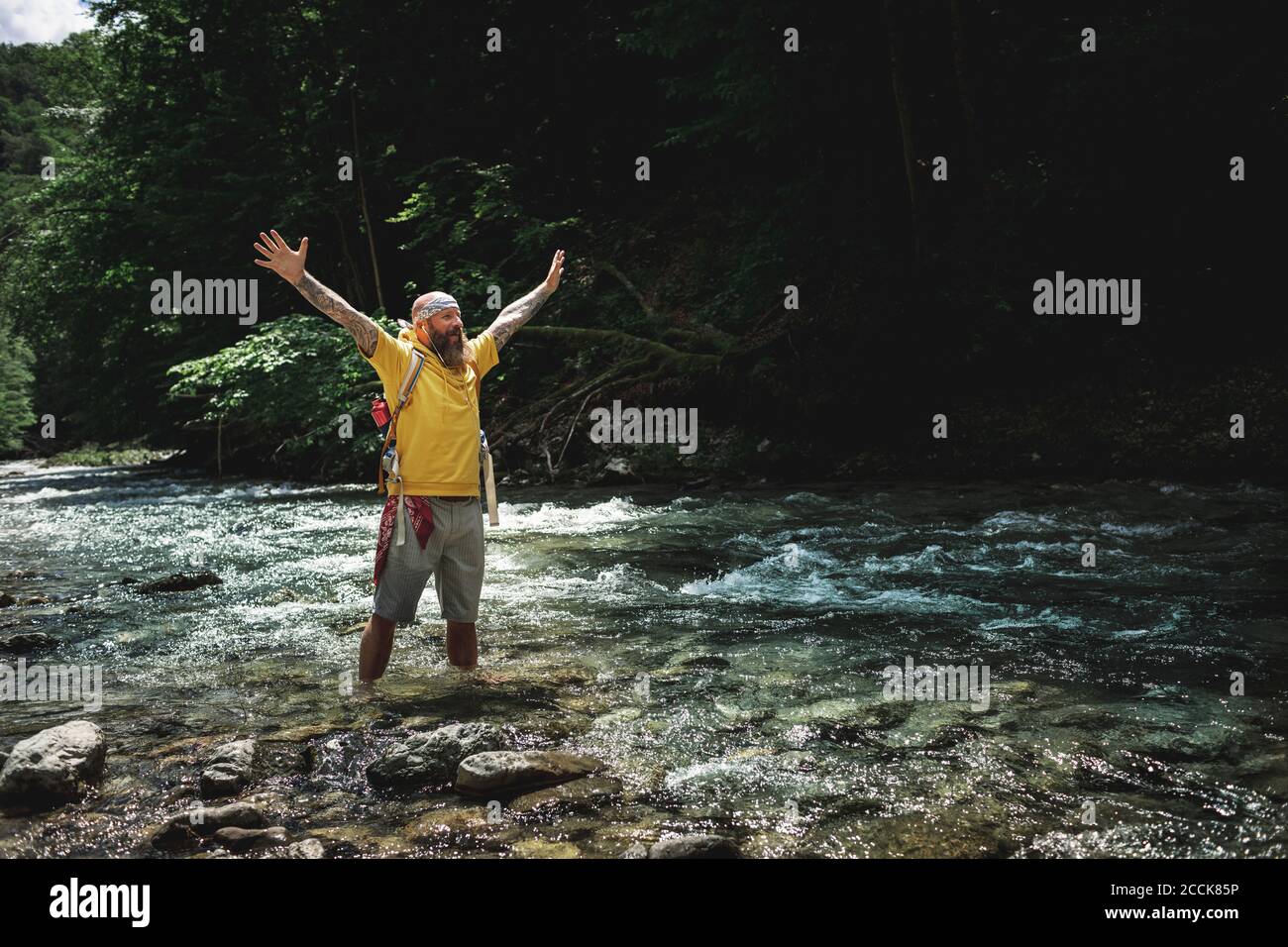 Walker avec une barbe complète et un sweat à capuche jaune debout en montagne rivière et bras de levage Banque D'Images