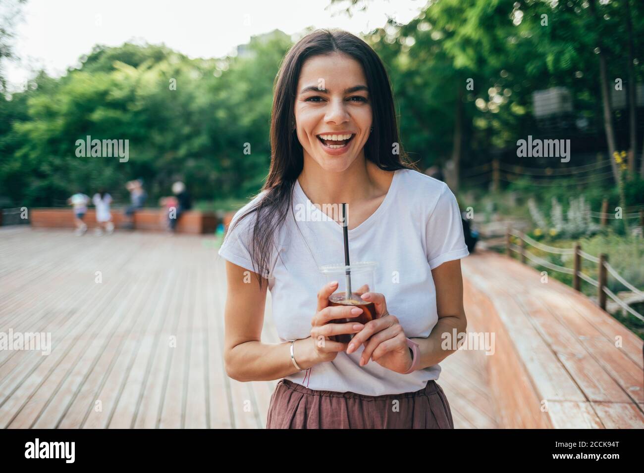 Jeune femme gaie tenant une tasse de boisson douce tout en restant debout stationnement Banque D'Images