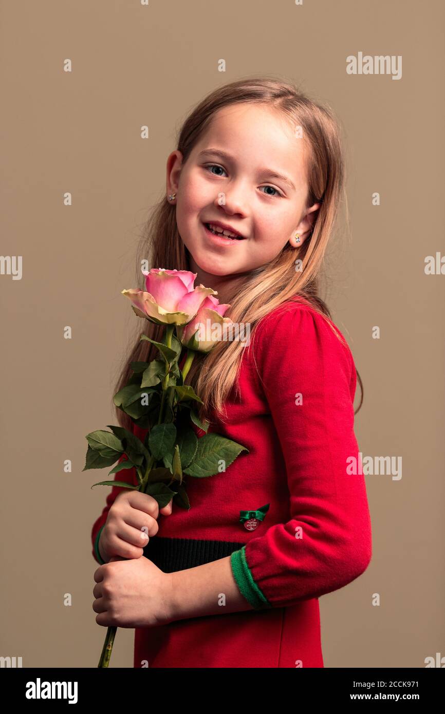 Jeune jolie fille de 8 ans vêtue d'une robe rouge tenant des fleurs isolées sur fond de couleur orange Banque D'Images