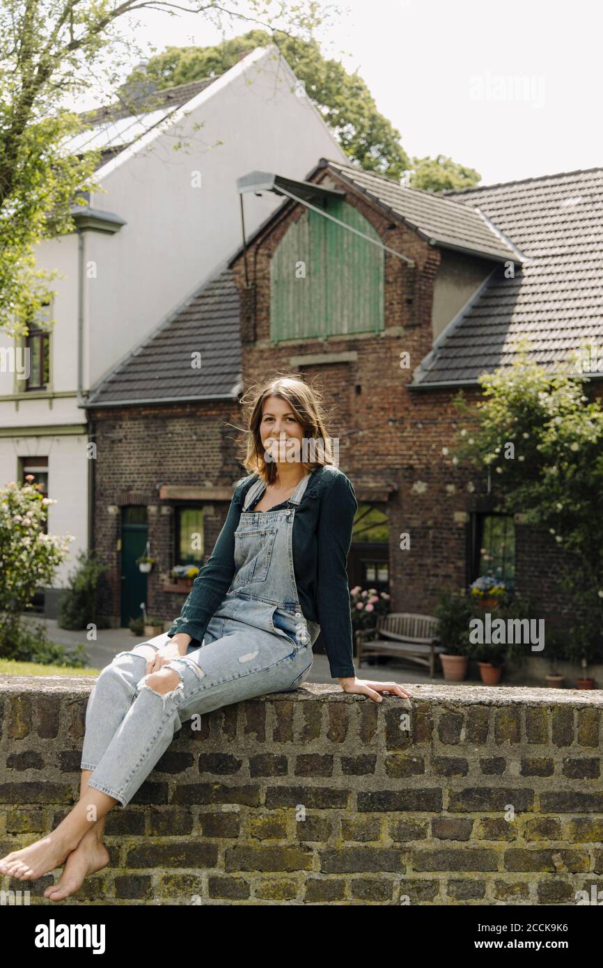 Portrait d'une jeune femme souriante assise sur un mur de briques dans une ferme Banque D'Images