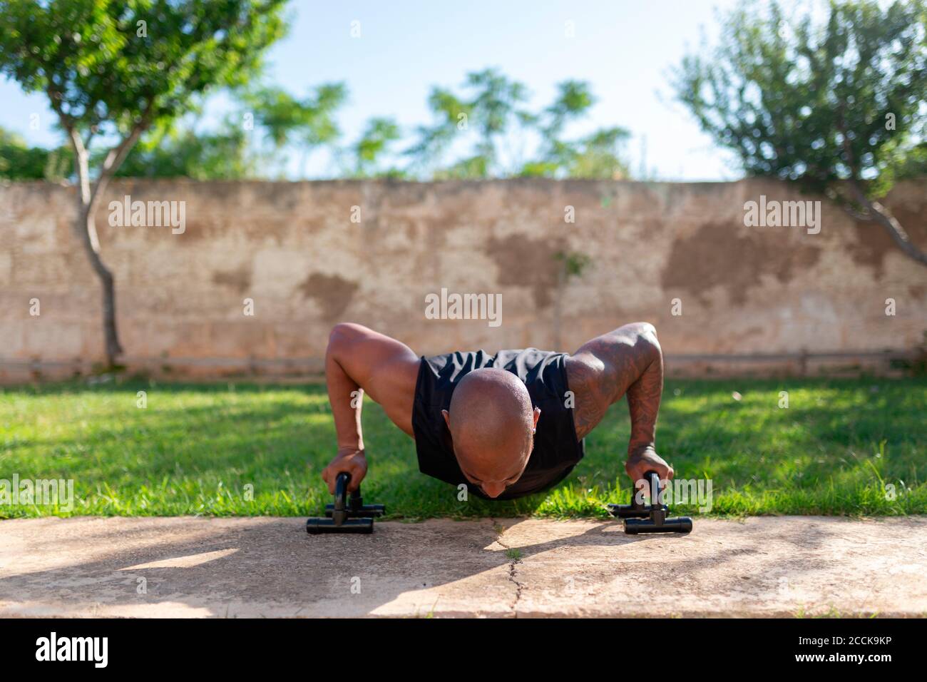 Homme mûr avec tête rasée pratiquant des push-up sur les terres herbeuses dans la cour Banque D'Images