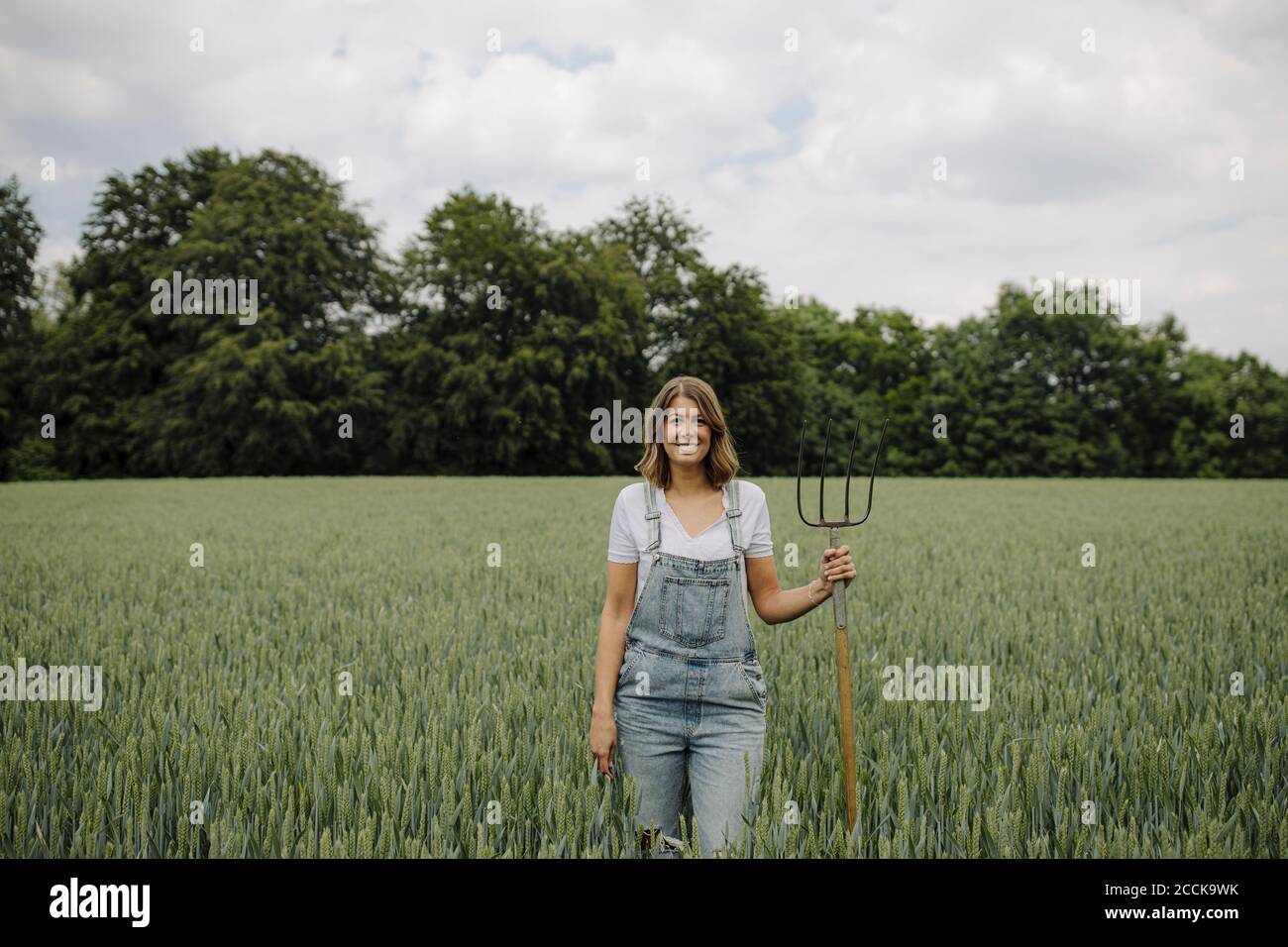 Jeune femme avec fourche de foin debout dans un champ de grain dans la campagne Banque D'Images