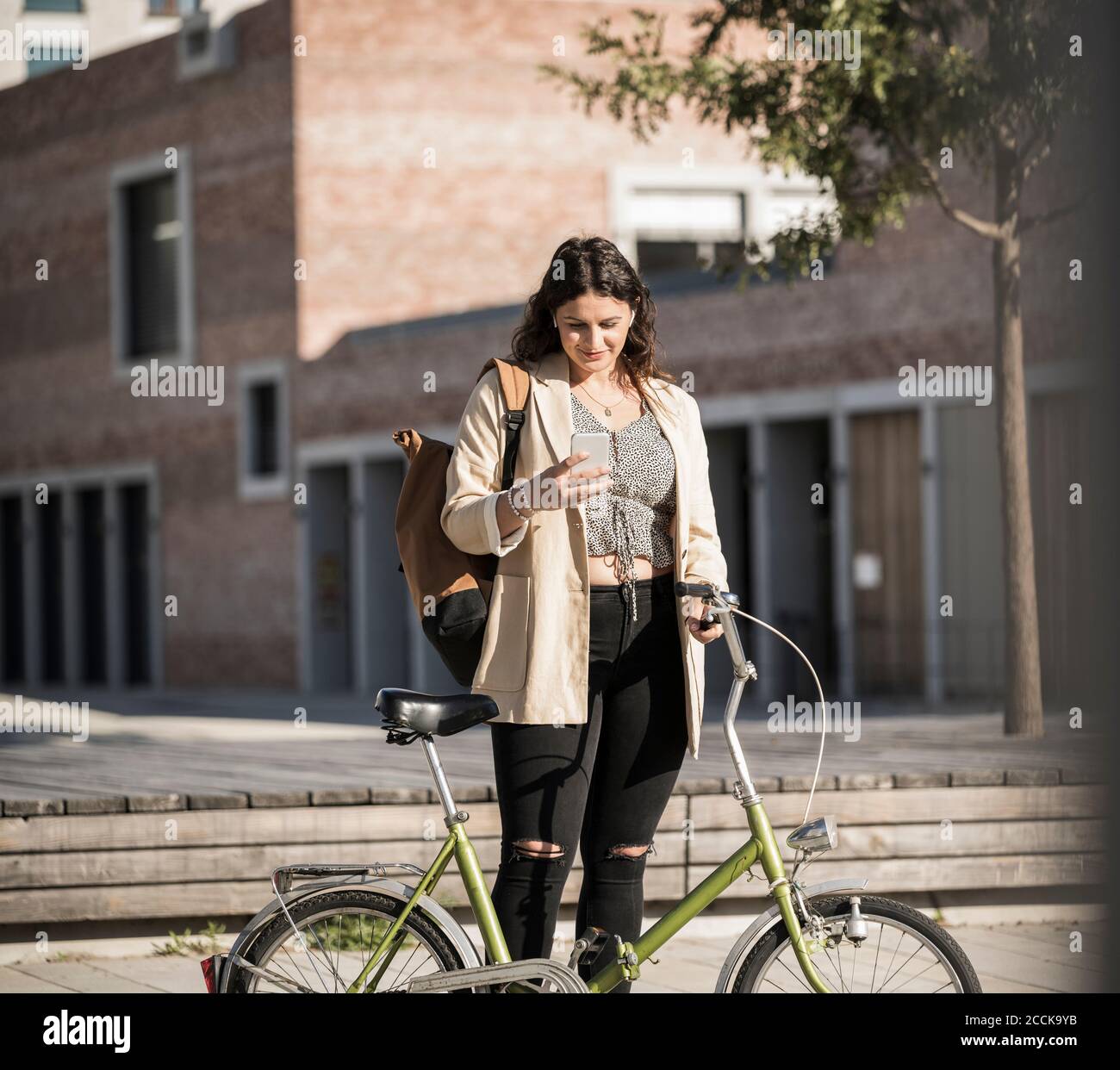 Jeune femme utilisant un smartphone debout à vélo rue de la ville Banque D'Images