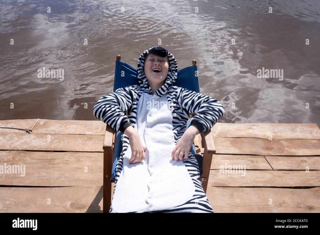 Garçon souriant en costume de zébré assis sur une chaise au bord du lac Banque D'Images