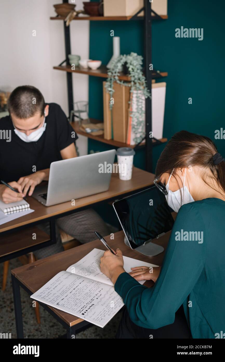 Un jeune homme et une jeune femme portant un masque de protection travaillant sur un bureau à la maison Banque D'Images