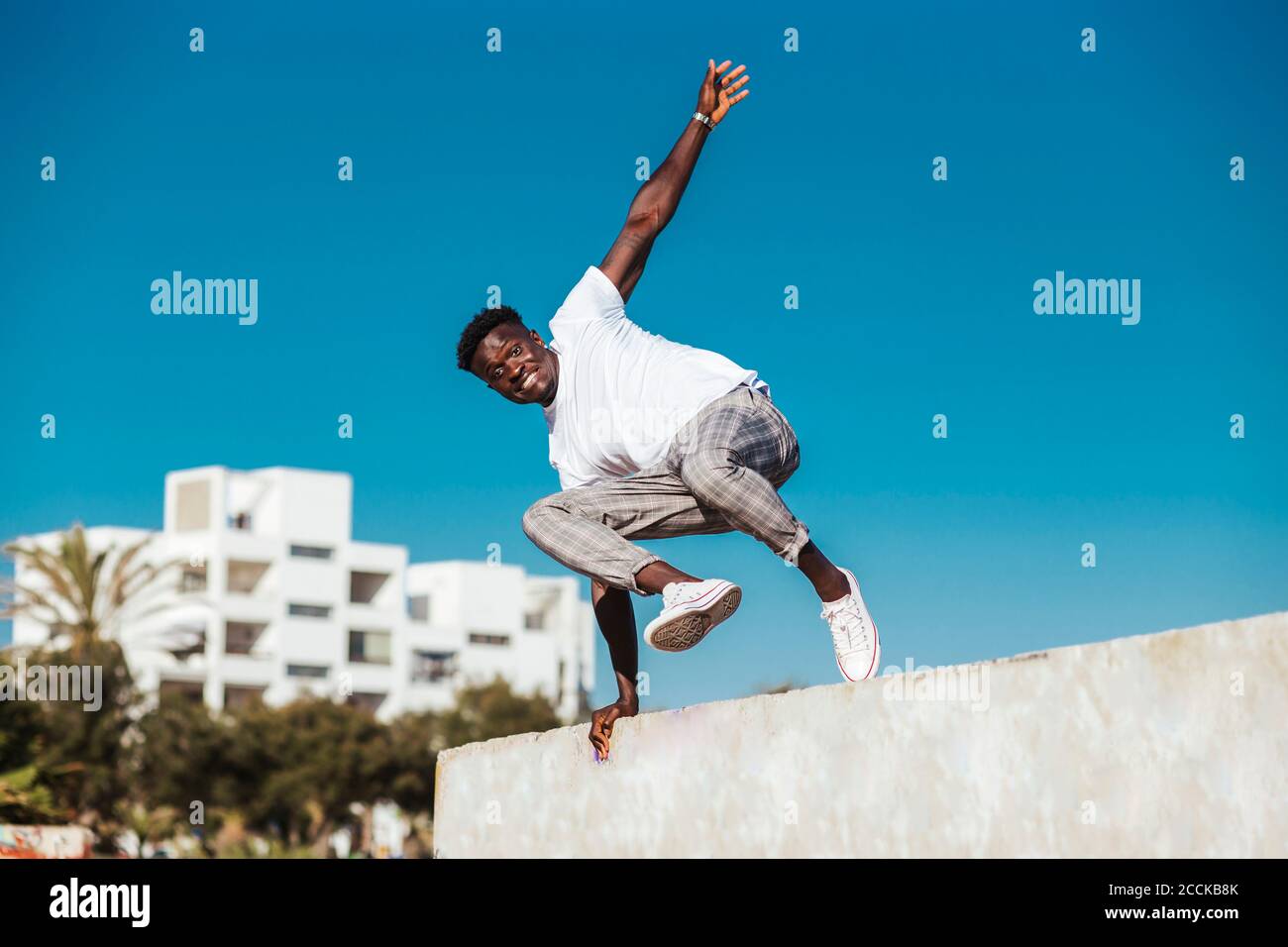 Homme africain sautant par-dessus le mur de soutènement contre le ciel bleu clair par beau temps Banque D'Images