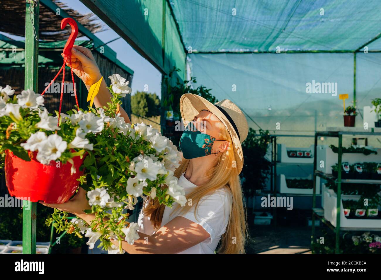Femme adulte de taille moyenne portant un masque et un chapeau accrochant des fleurs pépinière Banque D'Images