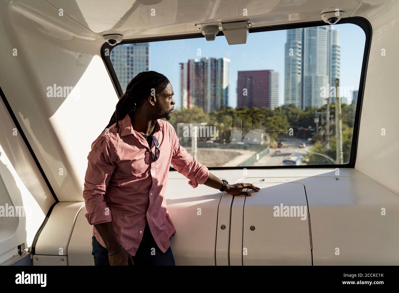 Jeune homme avec des dreadlocks regardant par la fenêtre en train, Miami, Floride, États-Unis Banque D'Images