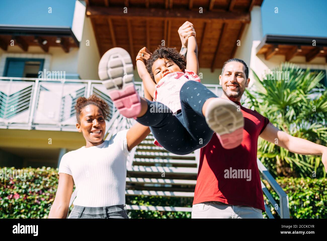 Des parents heureux tenant les mains de la fille ludique et la ramasser contre maison Banque D'Images