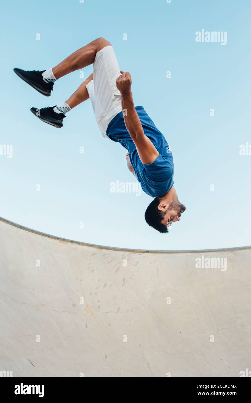 Un jeune homme qui fait du wallflip sur une rampe de sport contre un ciel dégagé Banque D'Images