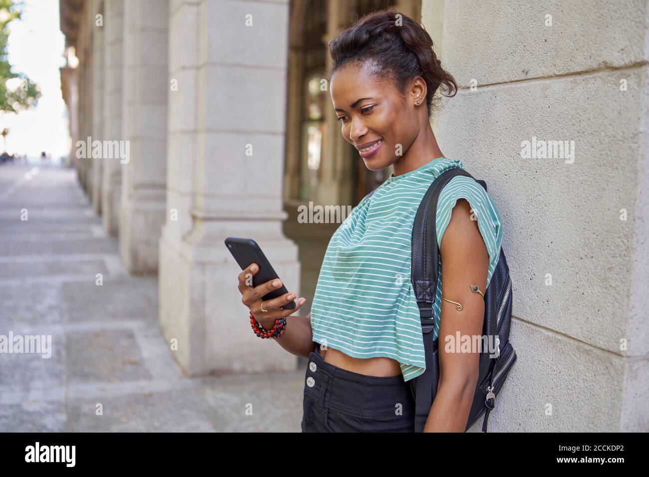 Femme souriante utilisant le téléphone tout en se tenant contre la colonne dans la ville Banque D'Images Femme souriante utilisant le téléphone tout en se tenant contre la colonne dans la ville Banque D'Images