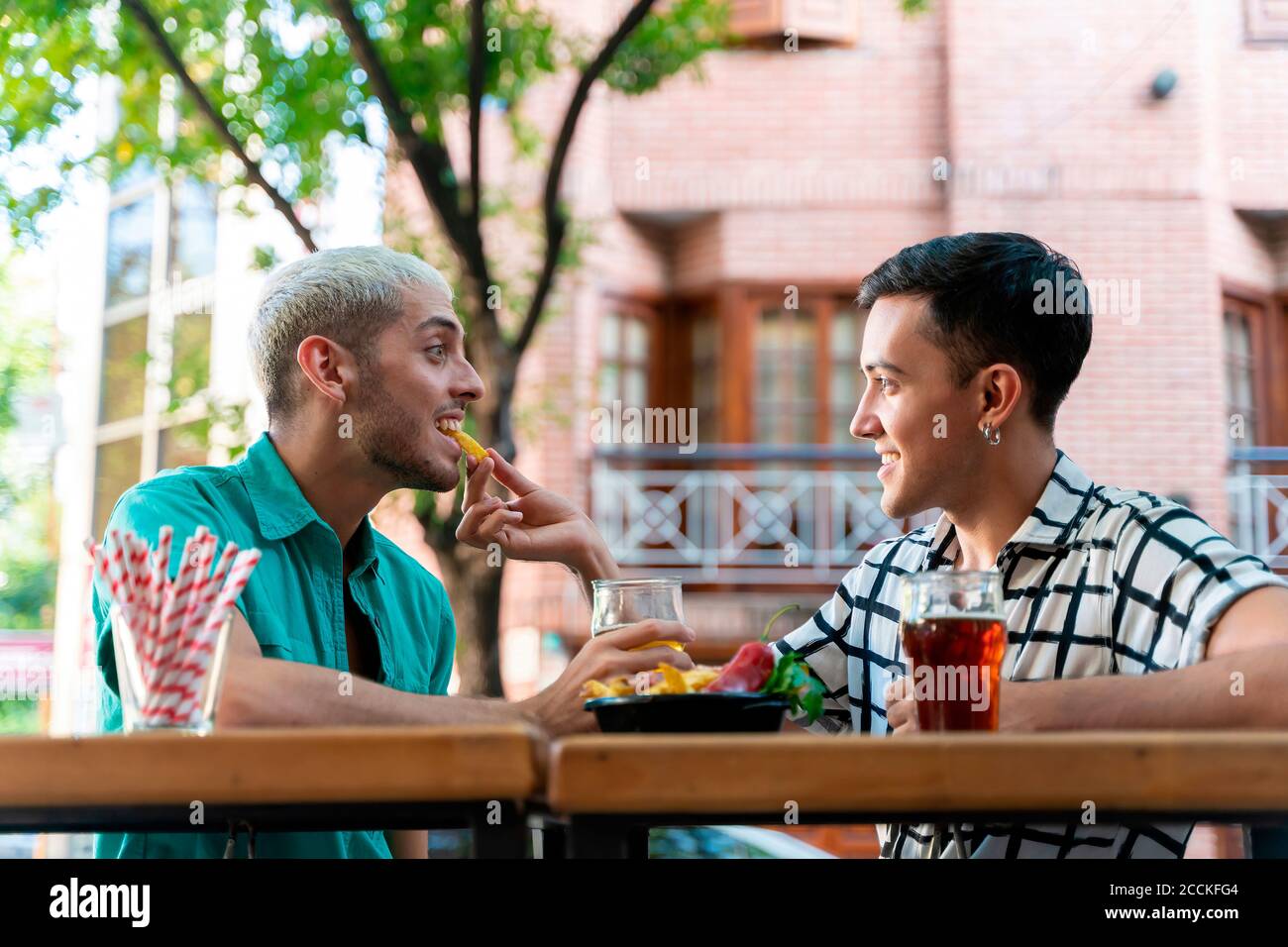 Un homme gay souriant qui se nourrit de sa partenaire tout en étant assis au comptoir du bar dans le restaurant Banque D'Images