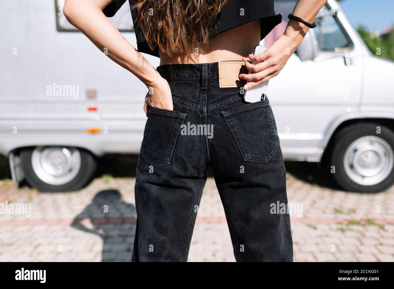 Jeune femme mettant un smartphone dans la poche de son pantalon Banque D'Images