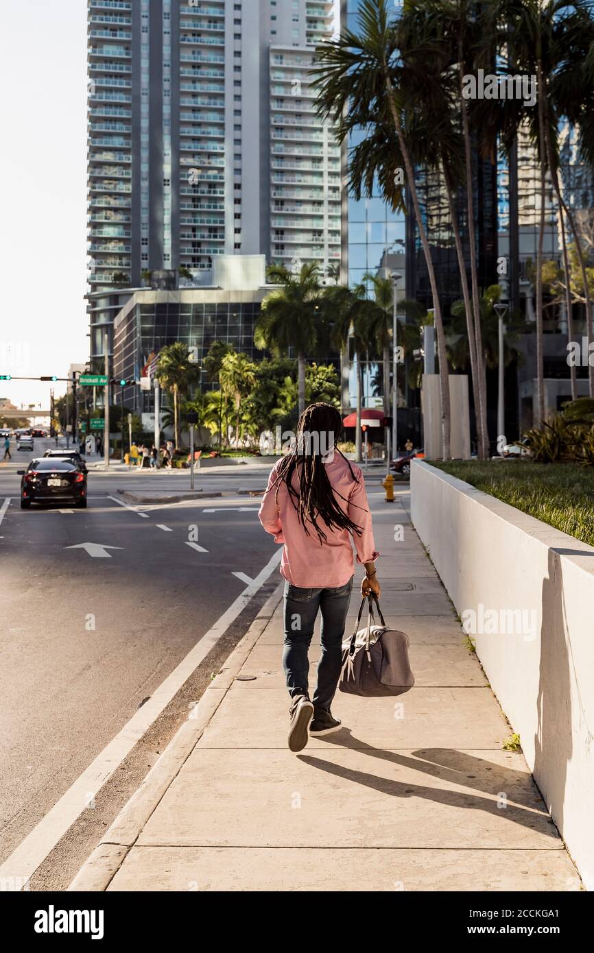 Afro homme avec des dreadlocks tenant le sac tout en marchant sur le trottoir dans la ville de Miami, Floride, États-Unis Banque D'Images