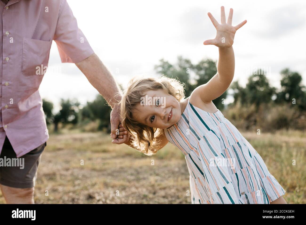 Jolie fille gaie tenant la main du grand-père tout en étant debout sur la terre contre le ciel Banque D'Images