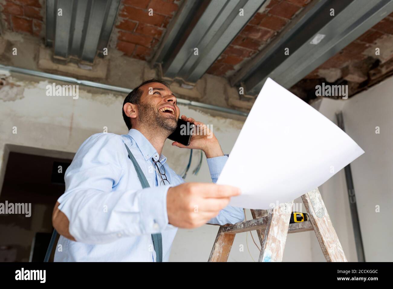 Un architecte riant avec plan au téléphone dans une maison en construction Banque D'Images