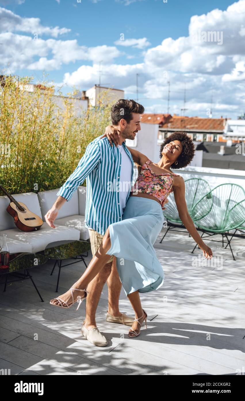 Couple multiethnique dansant sur le patio de l'appartement-terrasse pendant la journée ensoleillée Banque D'Images