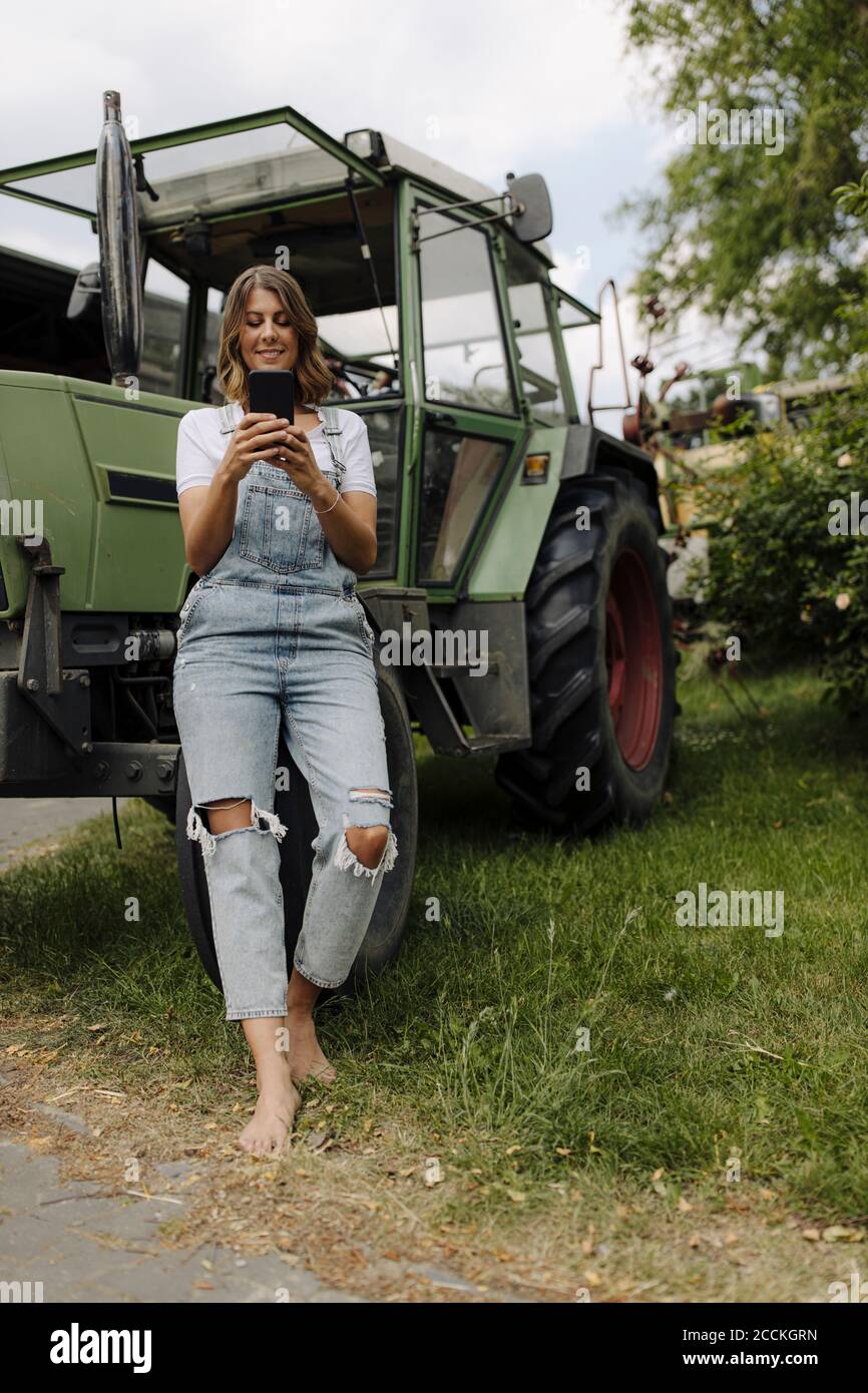 Jeune femme utilisant un téléphone portable à un tracteur dans le campagne Banque D'Images