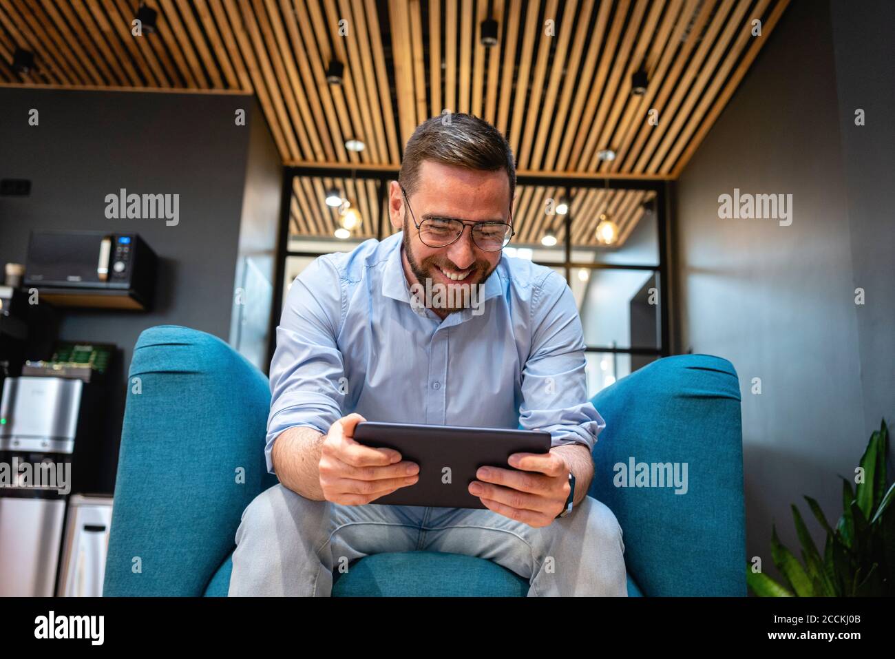 Homme joyeux professionnel utilisant une tablette numérique pour les appels vidéo pendant assis sur un fauteuil à la cafétéria du bureau Banque D'Images