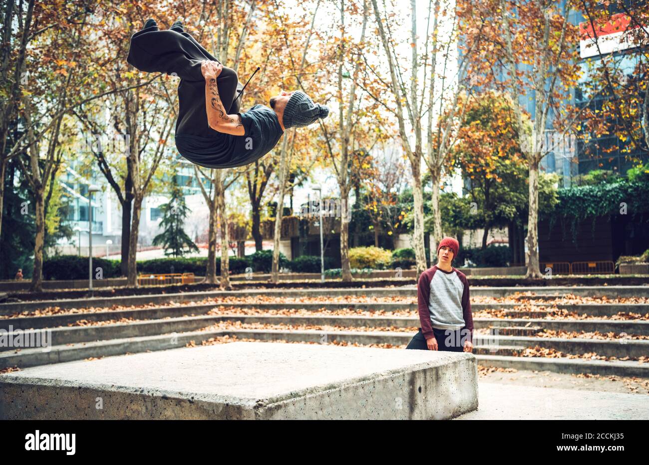 Un jeune homme sautant alors qu'un ami regarde dans un parc public Banque D'Images
