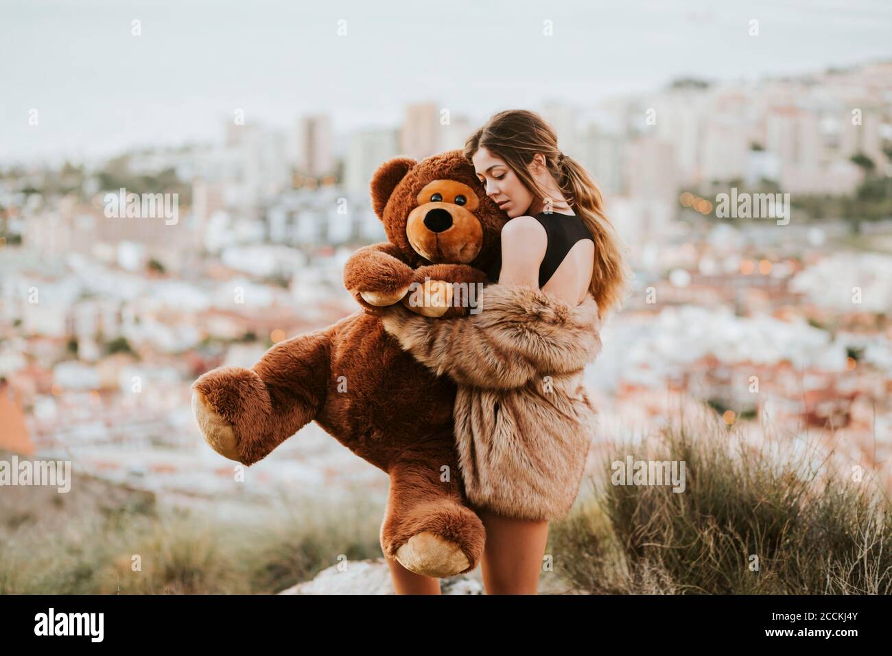 Femme avec les yeux fermés embrassant l'ours en peluche tout en se tenant contre ville Banque D'Images
