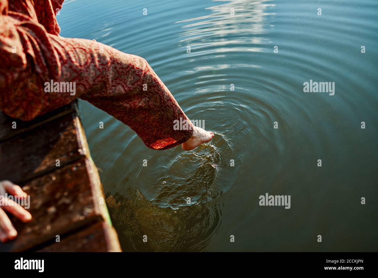 Femme assise sur la jetée d'un lac touchant l'eau avec son pied Banque D'Images