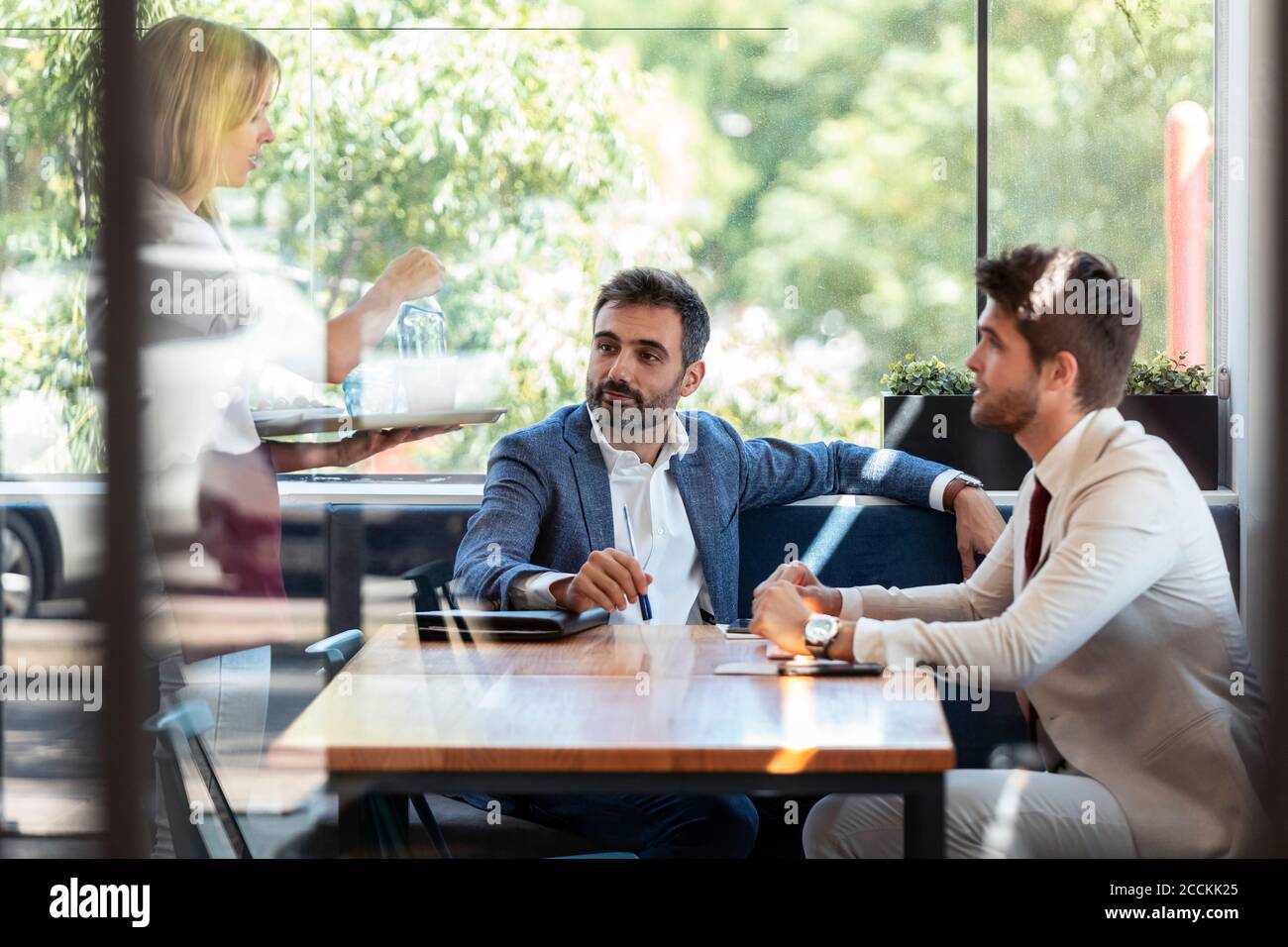 Hommes d'affaires assis à table donnant ordre à serveuse au restaurant Banque D'Images Hommes d'affaires assis à table donnant ordre à serveuse au restaurant Banque D'Images