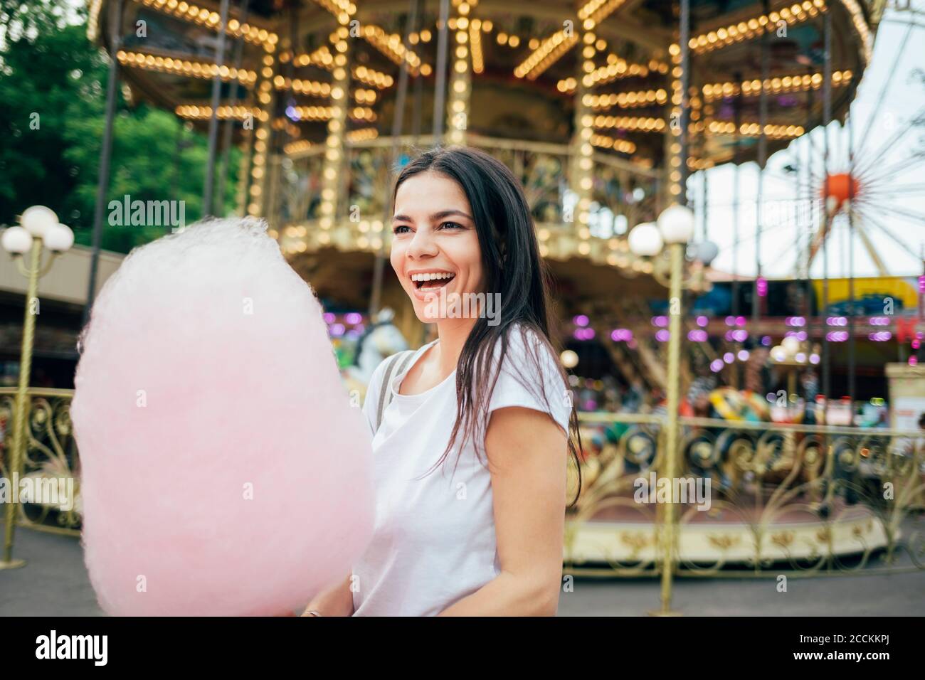 Jeune femme joyeuse avec des bonbons en coton debout dans le parc d'attractions Banque D'Images