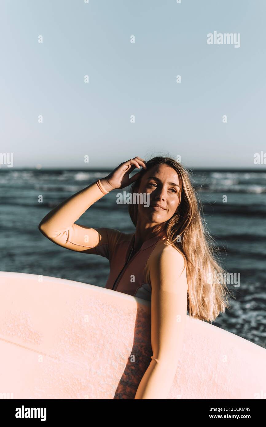 Jeune femme portant une planche de surf, regardant loin tout en se tenant contre la mer Banque D'Images