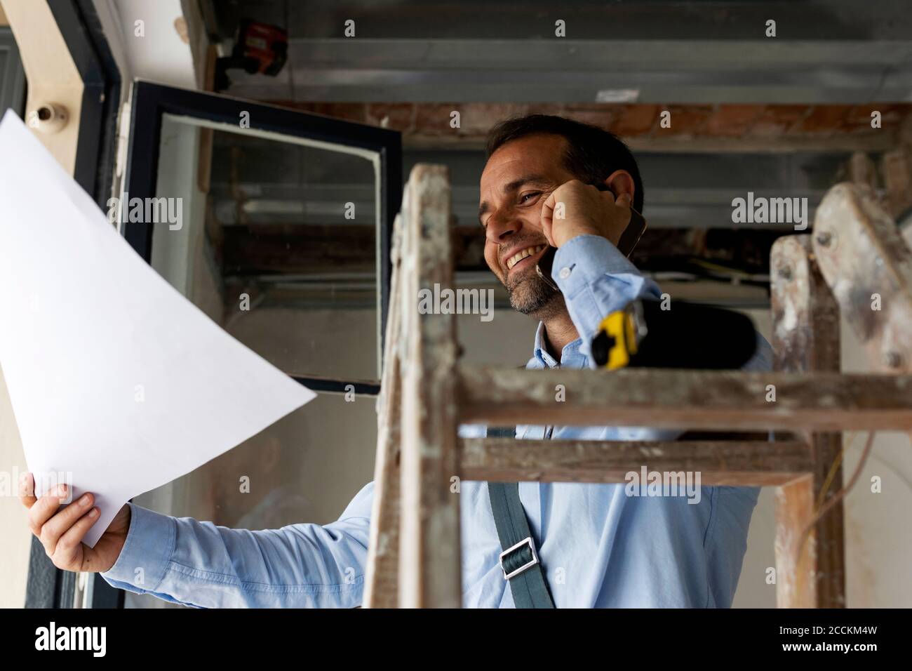 Architecte souriant avec plan au téléphone dans une maison en construction Banque D'Images