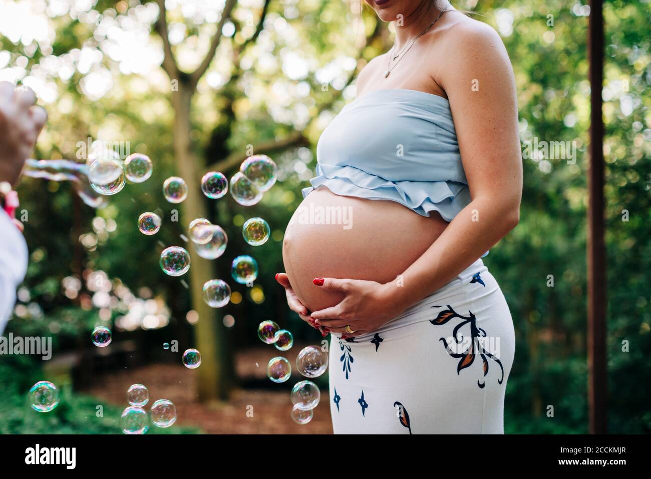 Femme enceinte avec les mains sur le ventre debout par des bulles à parc public Banque D'Images