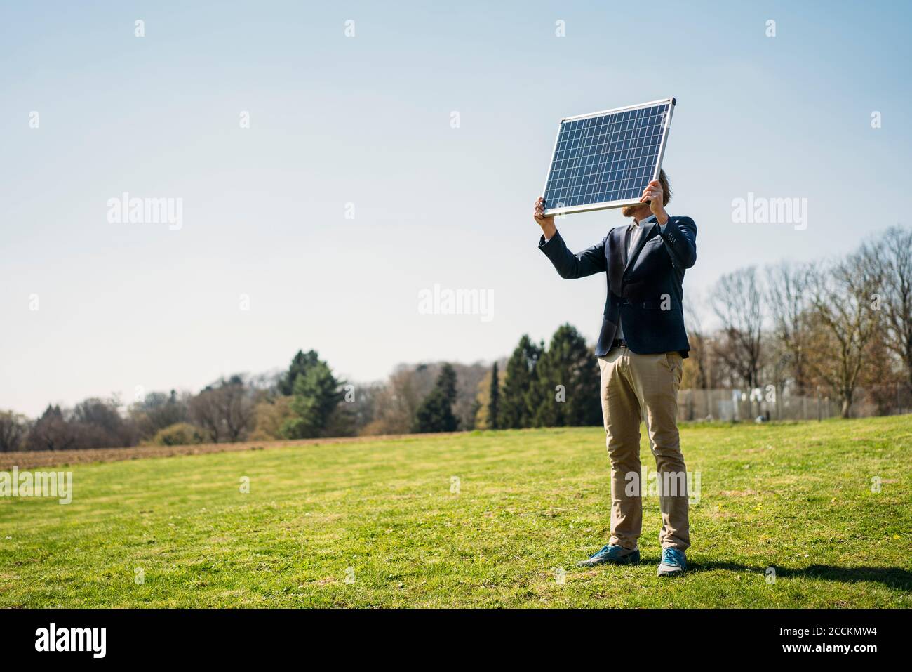 Homme professionnel tenant le panneau solaire en se tenant debout sur l'herbe à garez-vous dans un ciel dégagé par temps ensoleillé Banque D'Images