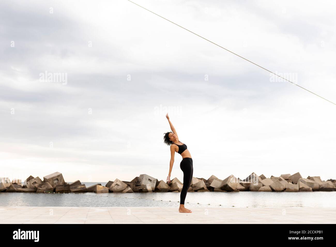 Femme adulte moyenne s'exerçant sur la promenade par mer contre le ciel nuageux ciel Banque D'Images