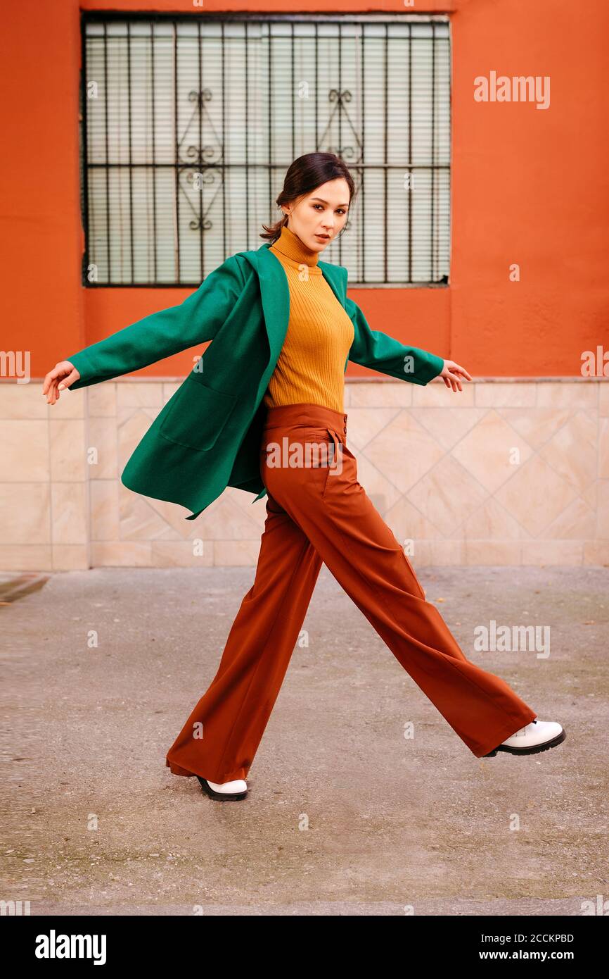 Jeune femme portant une veste verte marchant sur le sentier contre le bâtiment en ville Banque D'Images
