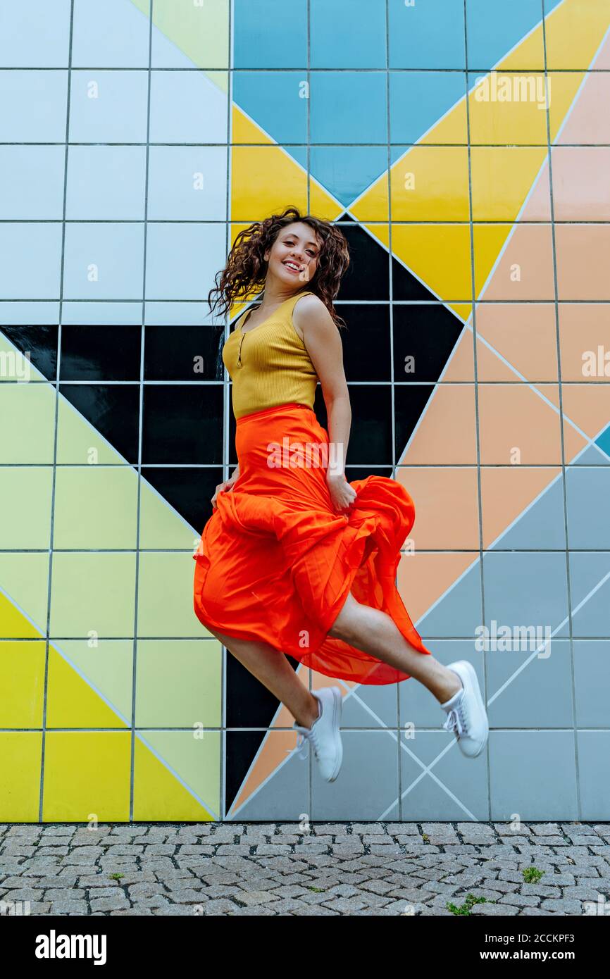 Une jeune femme sautant devant un mur carrelé coloré Banque D'Images