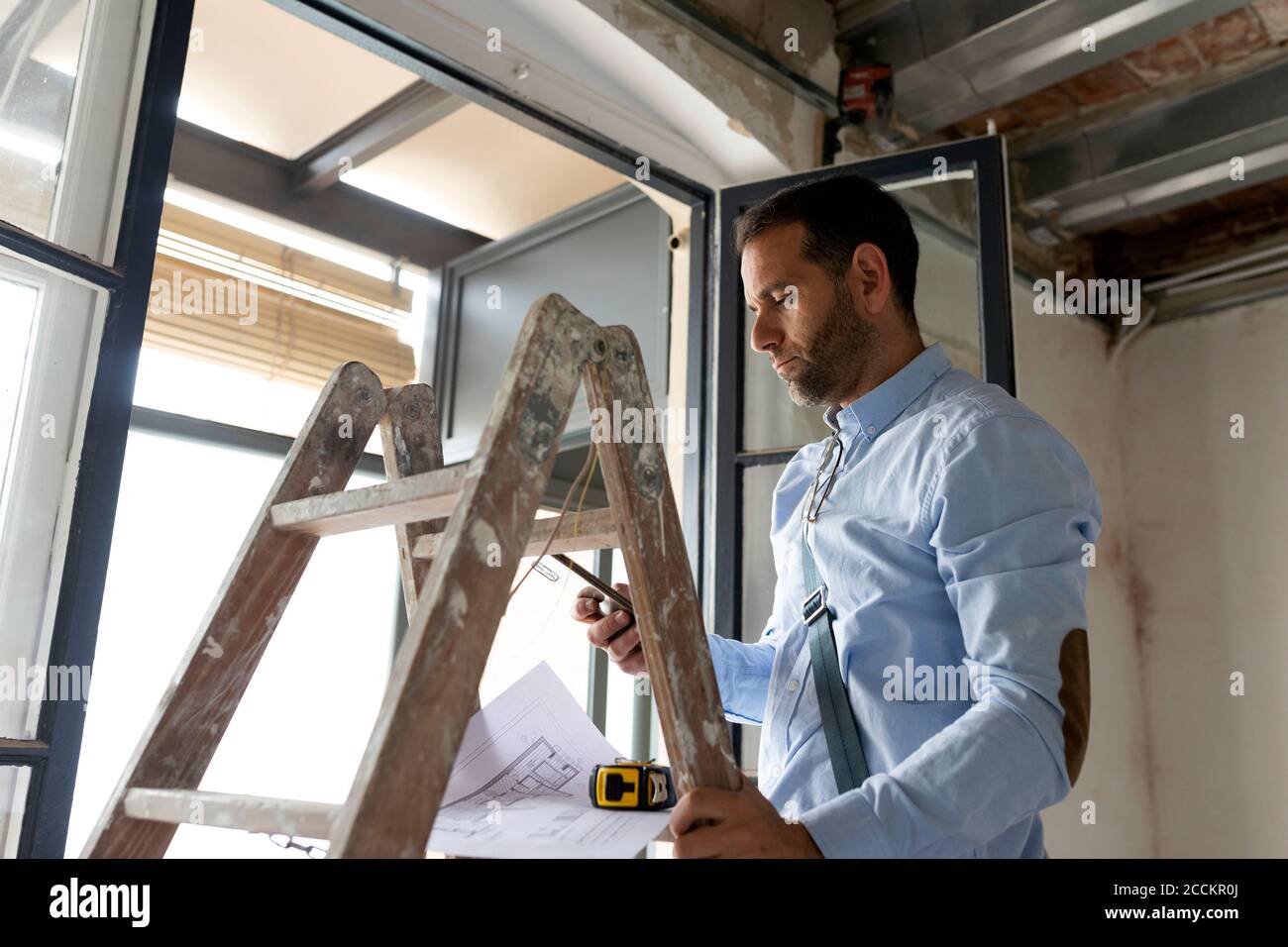 Architecte avec plan et téléphone mobile dans une maison sous construction Banque D'Images