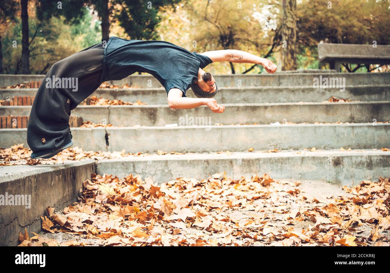 Un jeune homme sautant sur les feuilles d'automne dans un parc public Banque D'Images
