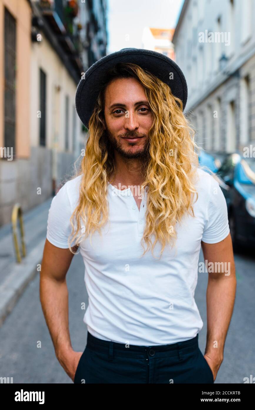 Homme mi-adulte élégant avec de longs cheveux portant un chapeau pendant en ville Banque D'Images