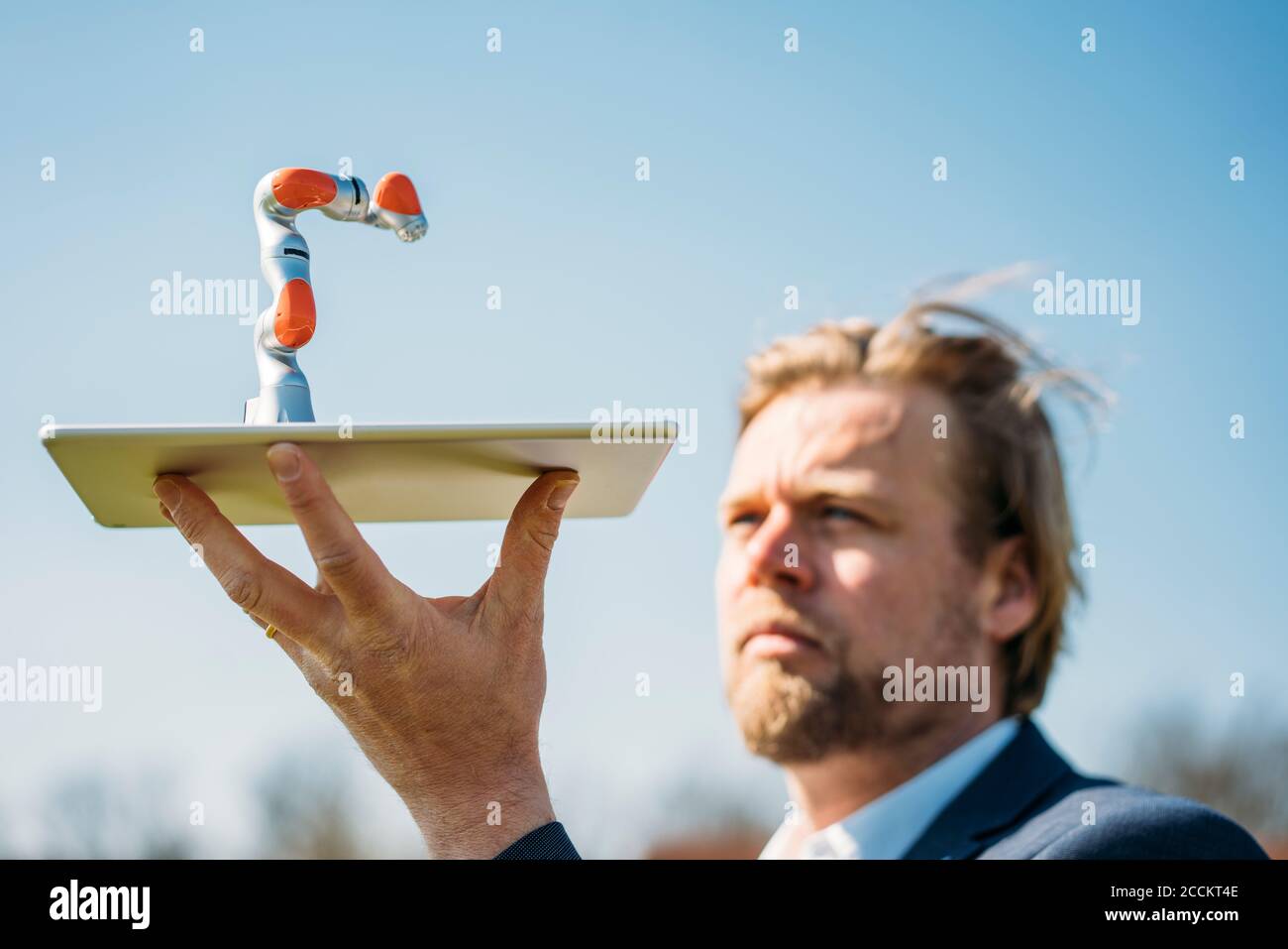 Homme professionnel tenant au petit bras robotique sur une tablette numérique contre le ciel dégagé Banque D'Images