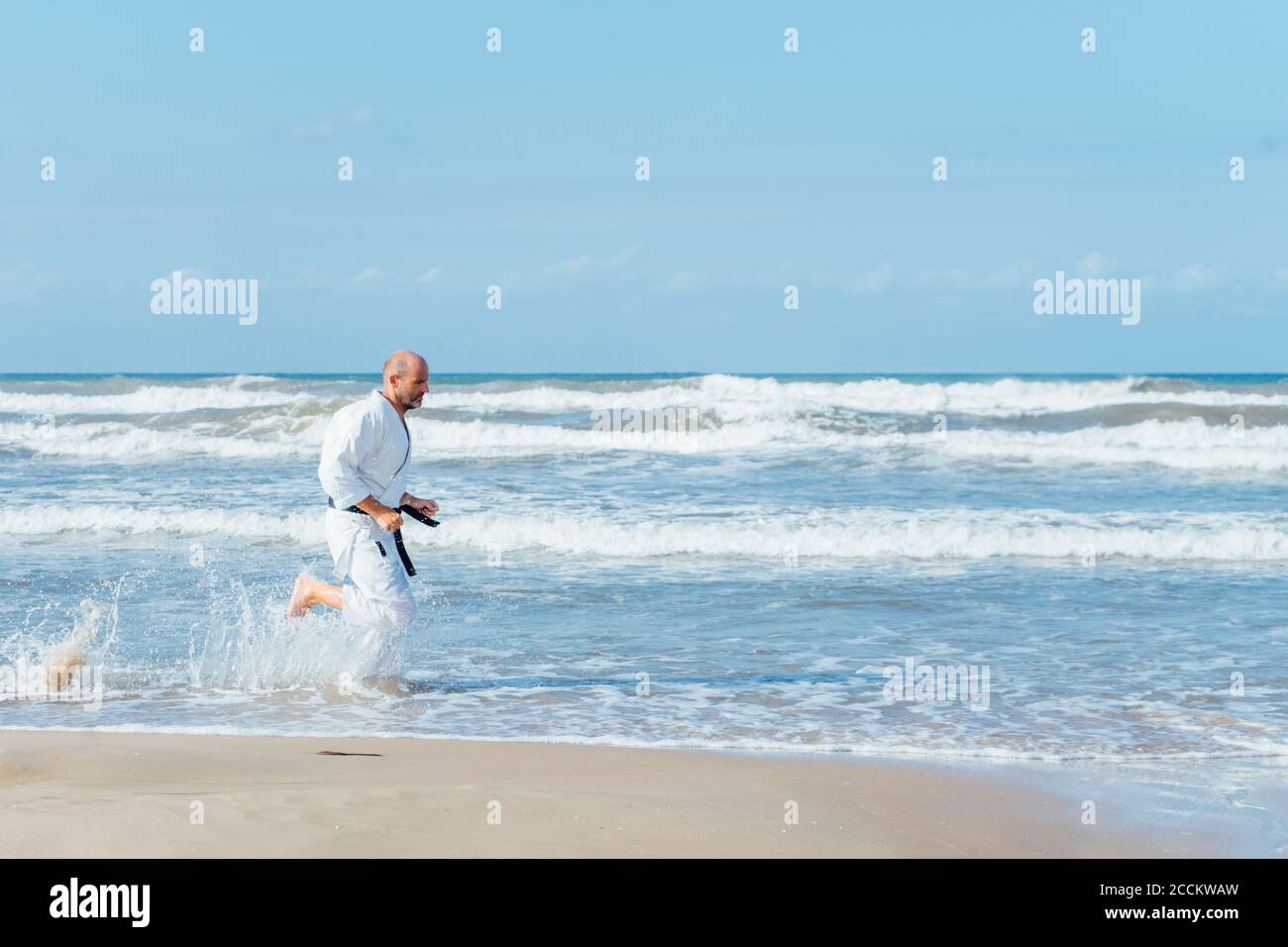 Homme mature portant gi courant à la plage contre le ciel pendant jour ensoleillé Banque D'Images