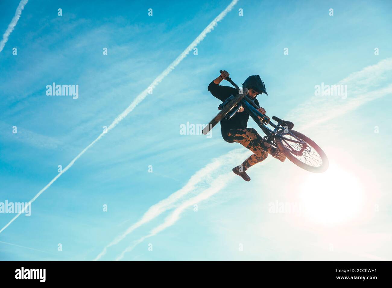 Un homme sans souci sautant tout en effectuant des cascades avec vélo contre bleu ciel au coucher du soleil Banque D'Images